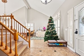 Un escalier menant à un espace de vie décoré d’un sapin de Noël, une porte avec des panneaux de verre et un meuble à chaussures.
