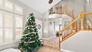 A spacious foyer with a large Christmas tree, a wooden staircase, and a view of the living area.