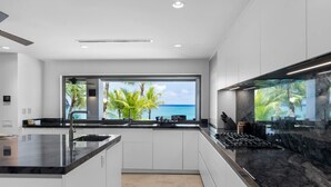 A modern kitchen with a large window offering a view of palm trees and the ocean. - Newly Renovated Notos Cove Villa Property (Nassau)