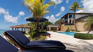 A resort with a pool, lounge chairs, and a thatched-roof structure. - Newly Renovated Notos Cove Villa Property (Nassau)