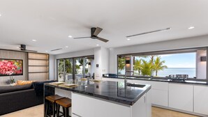 A modern kitchen with a large island, white cabinetry, and a view of the ocean. - Newly Renovated Notos Cove Villa Property (Nassau)