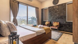 Ein Hotelzimmer mit einem großen Bett, einer Sitzecke mit zwei Stühlen, Blick auf die Berge und einer Steinwand.