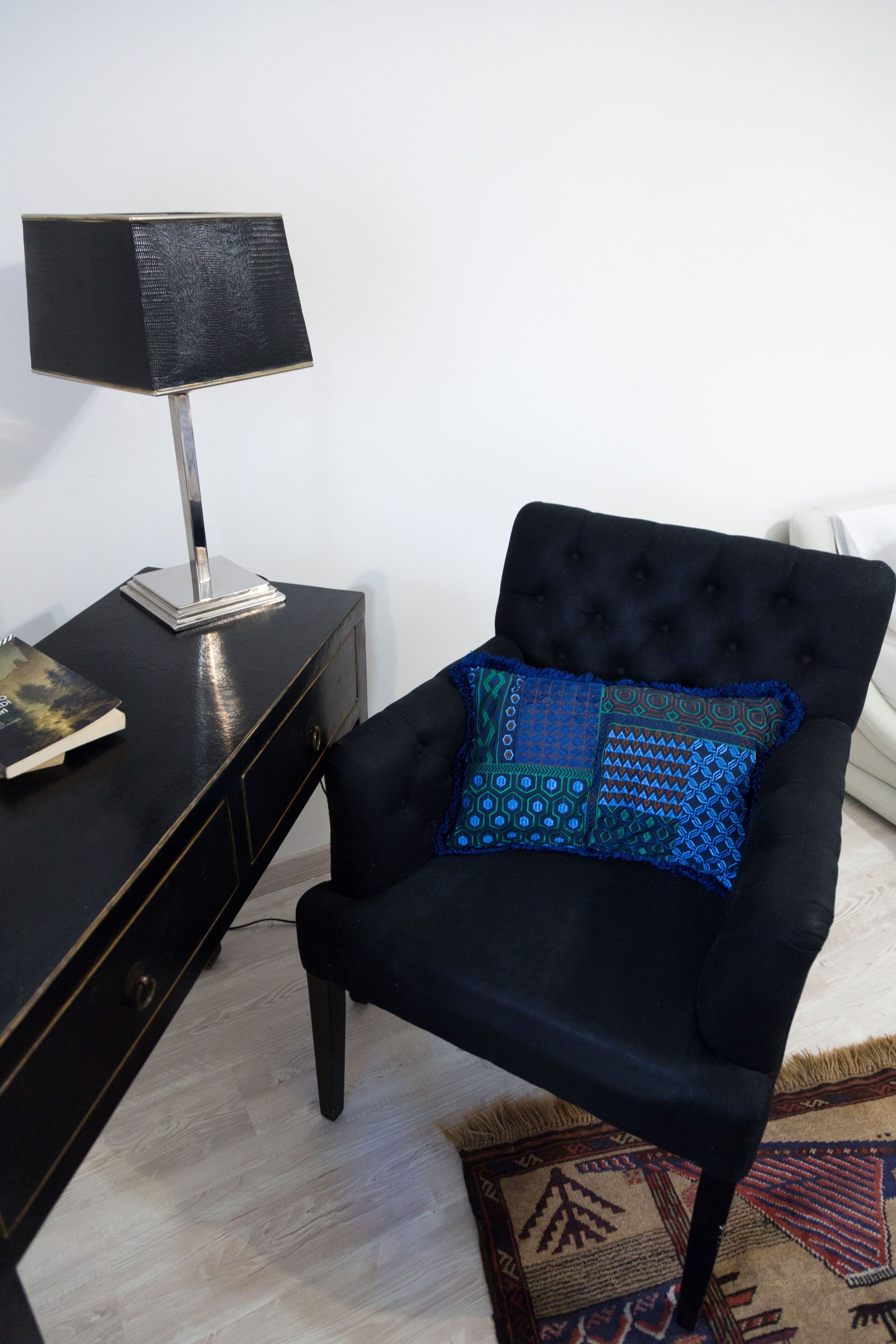 Un fauteuil noir avec un coussin à motifs, un bureau noir avec une lampe et un tapis à motifs.