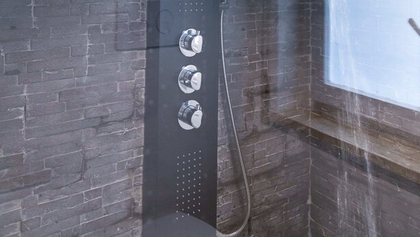 Una ducha moderna con diseño curvo, un panel de control con tres mandos y un chorro de agua visible.