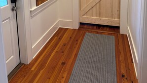 A hallway with a wooden door, a window with blinds, and a patterned rug.