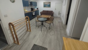 Un espace de vie compact comprenant un coin cuisine, un coin repas avec une table et des chaises, un canapé et un ventilateur.