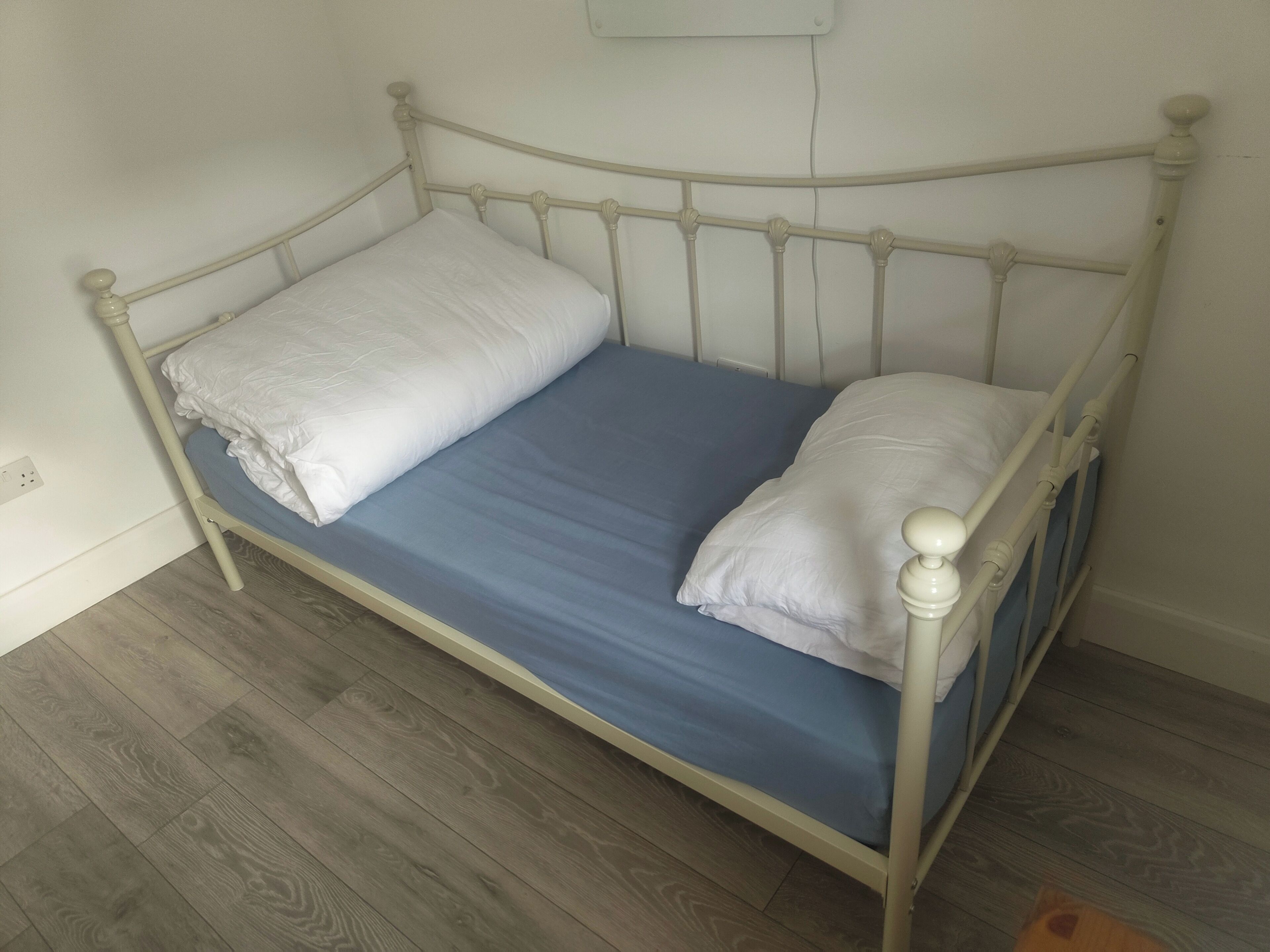 Un lit simple avec une tête de lit et un pied de lit blancs, un protège-matelas bleu et deux oreillers blancs.