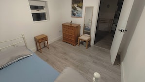 Une chambre à coucher avec un lit, une commode en bois, une petite table, un miroir et une fenêtre.