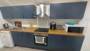 Une cuisine compacte avec des meubles bleus, une hotte de cuisinière en acier inoxydable, un four à micro-ondes, un grille-pain et un lave-vaisselle.