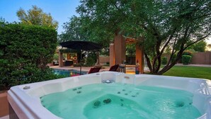 Un bain à remous dans un jardin, avec une piscine, entouré d’arbres et agrémenté d’un espace patio.