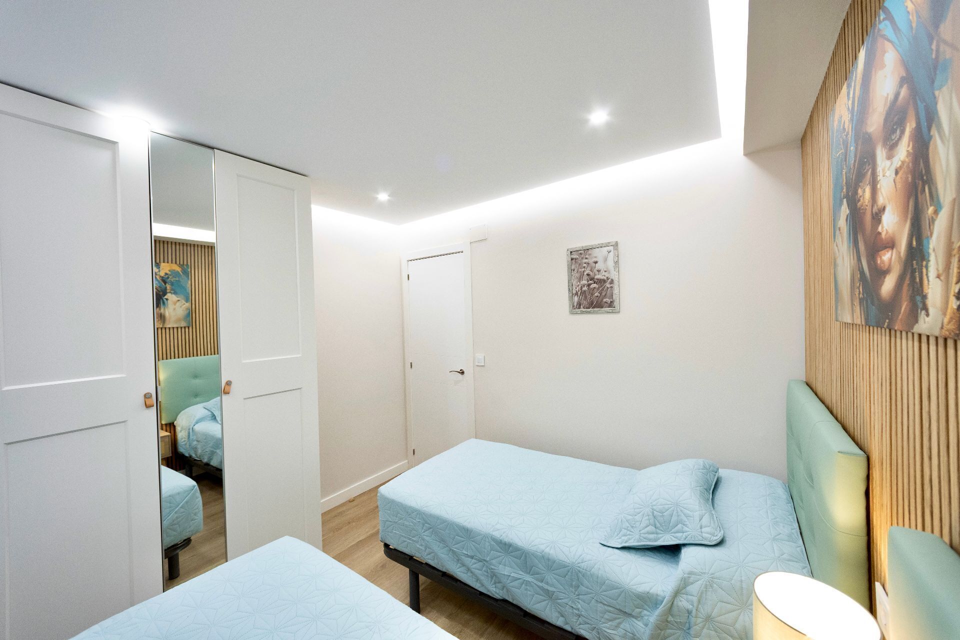 A bedroom with two single beds, a wardrobe, a mirror, and a painting on the wall.