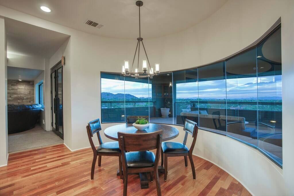 A modern dining area with a round table and chairs, large windows offering a view of the ocean and mountains, and a curved glass wall.