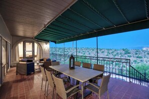 Eine überdachte Terrasse im Freien mit Tisch und Stühlen, Blick auf eine Wüstenlandschaft und eine Steinmauer.