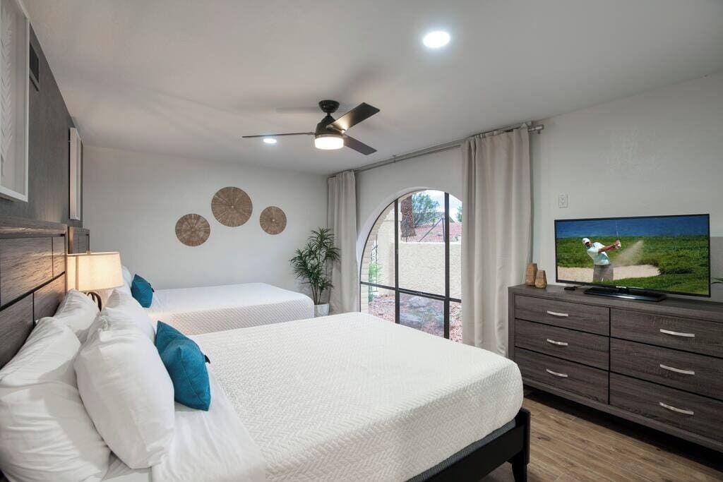 A hotel room with two beds, a ceiling fan, a TV, and a window with curtains.