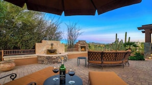 An outdoor patio with a stone fire pit, a table with wine glasses, and a wicker sofa. - The Refuge (Fountain Hills)
