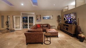 A spacious living room with a sectional sofa, a television, and a fireplace. - The Refuge (Fountain Hills)