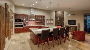 A modern kitchen with a central island, built-in appliances, and a dining area with bar stools. - The Refuge (Fountain Hills)