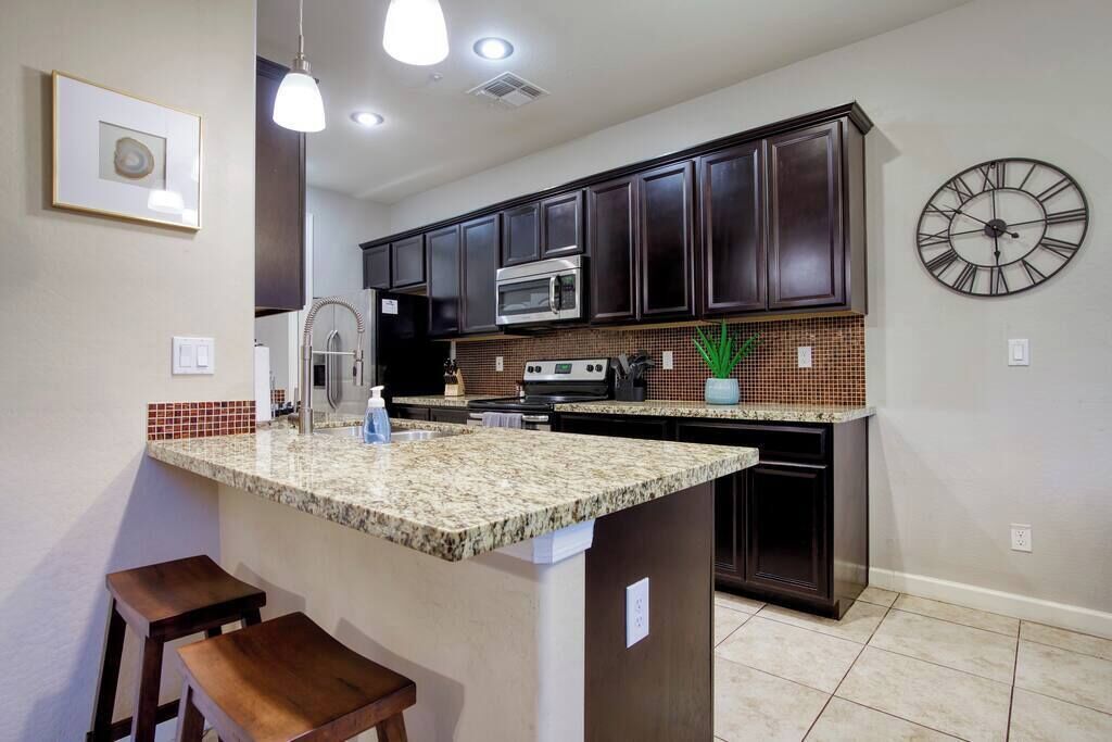 A kitchen with dark wood cabinets, a granite countertop, a stainless steel oven, and a wall clock.
