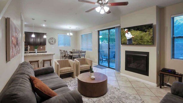 A modern living room with a gray sofa, a round coffee table, and a fireplace. There is a ceiling fan, a dining area with chairs, and a kitchen in the background. - Private Patio & Grill, 10 minutes to Old Town (Scottsdale)