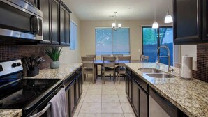 A modern kitchen with dark cabinetry, granite countertops, a built-in oven, and a dining area with a table and chairs. - Private Patio & Grill, 10 minutes to Old Town (Scottsdale)