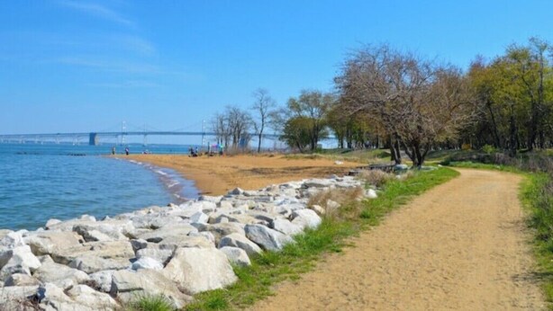 Un sendero costero con una playa de arena, un litoral rocoso y un puente al fondo.