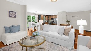 Una sala de estar moderna con un sofá blanco, una mesa de centro de vidrio y un comedor con una mesa y sillas blancas.