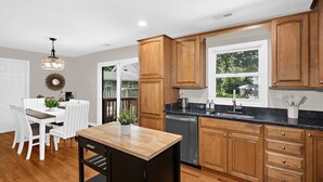 Una cocina moderna con armarios de madera, encimera negra y zona de comedor con sillas blancas.
