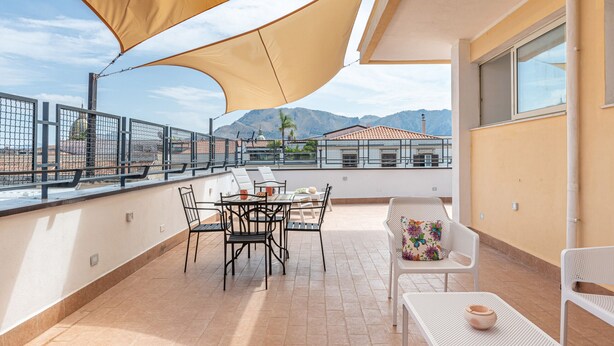 A rooftop terrace with a table and chairs, a large canopy, and a view of buildings and mountains in the background. - Casa 73 by Wonderful Italy (Palermo)