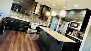 Una cocina moderna con suelo de madera oscura, una isla central, armarios oscuros e iluminación colgante.