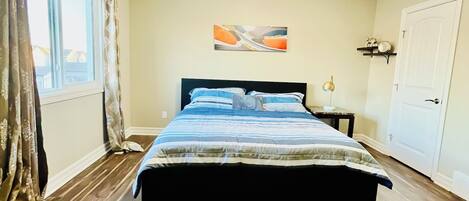 A bedroom with a bed, a nightstand, a wall-mounted shelf, a window with curtains, and a door.