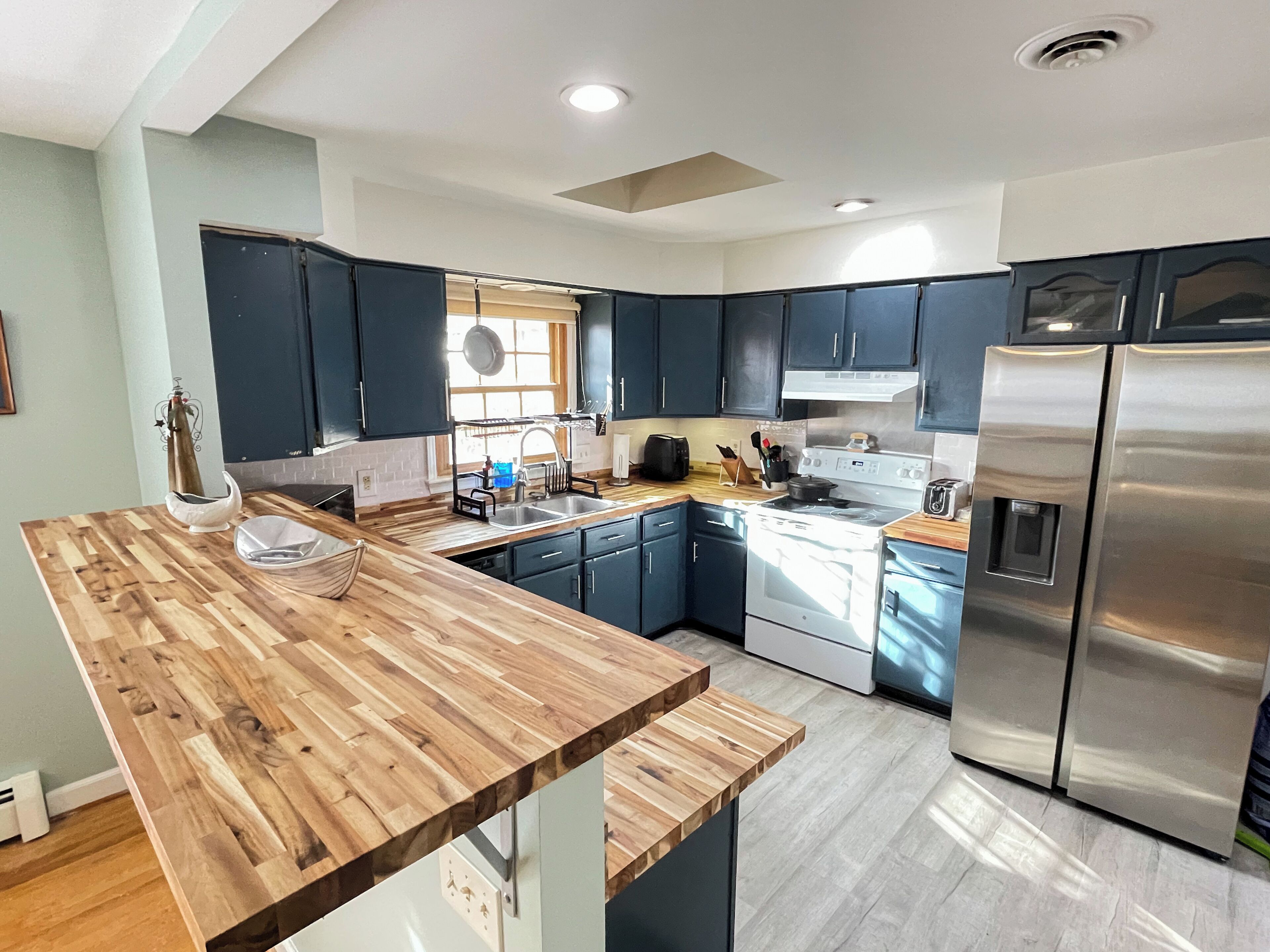 A modern kitchen with dark cabinets, a wooden countertop, stainless steel appliances, and a window providing natural light.