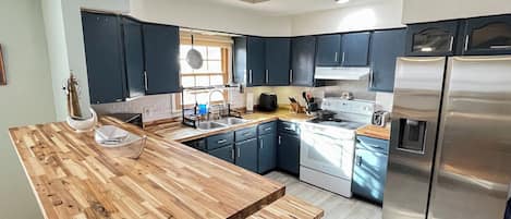 A modern kitchen with dark cabinets, a wooden countertop, stainless steel appliances, and a window providing natural light.