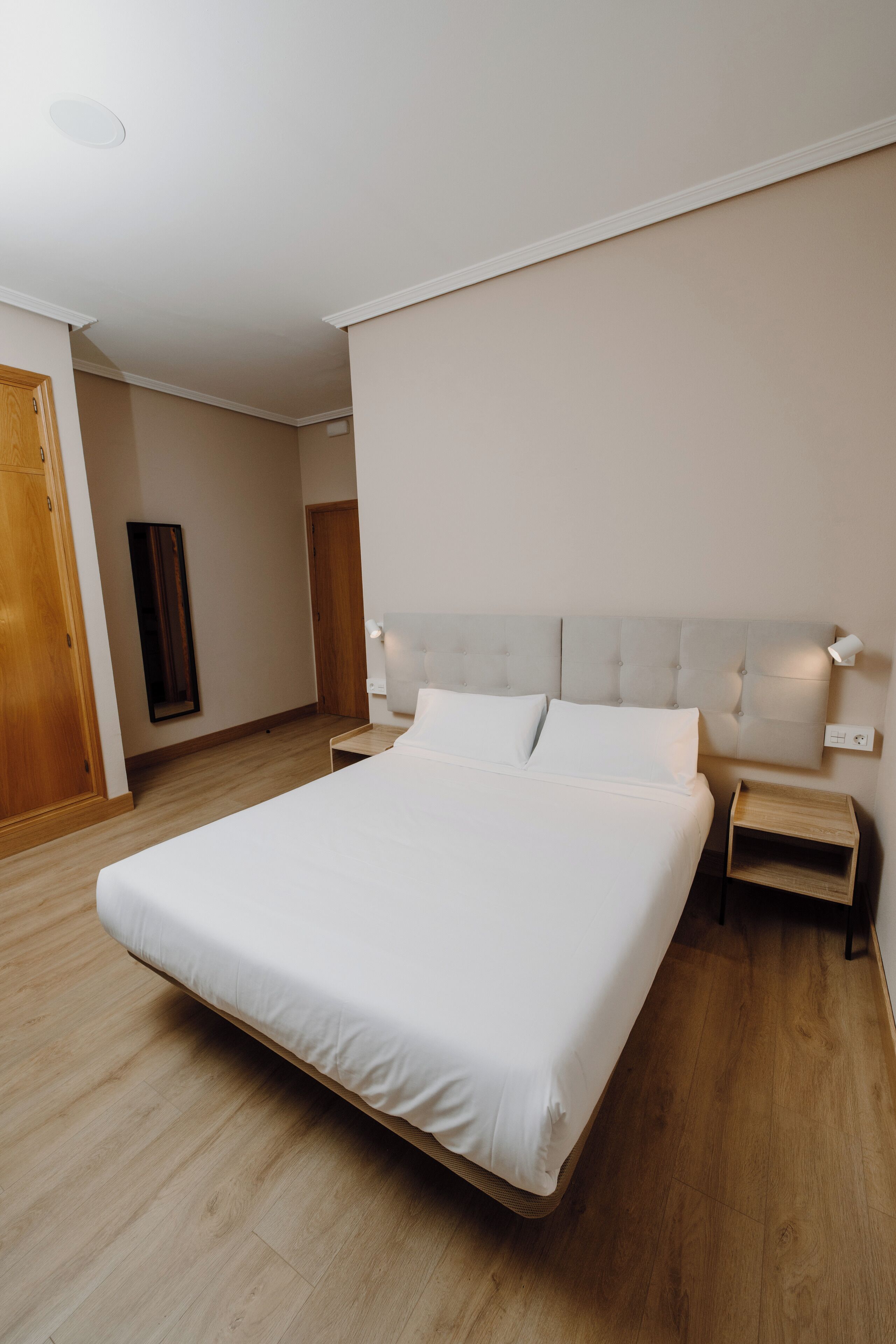 A spacious bedroom with a large bed, wooden flooring, and a neutral color scheme.