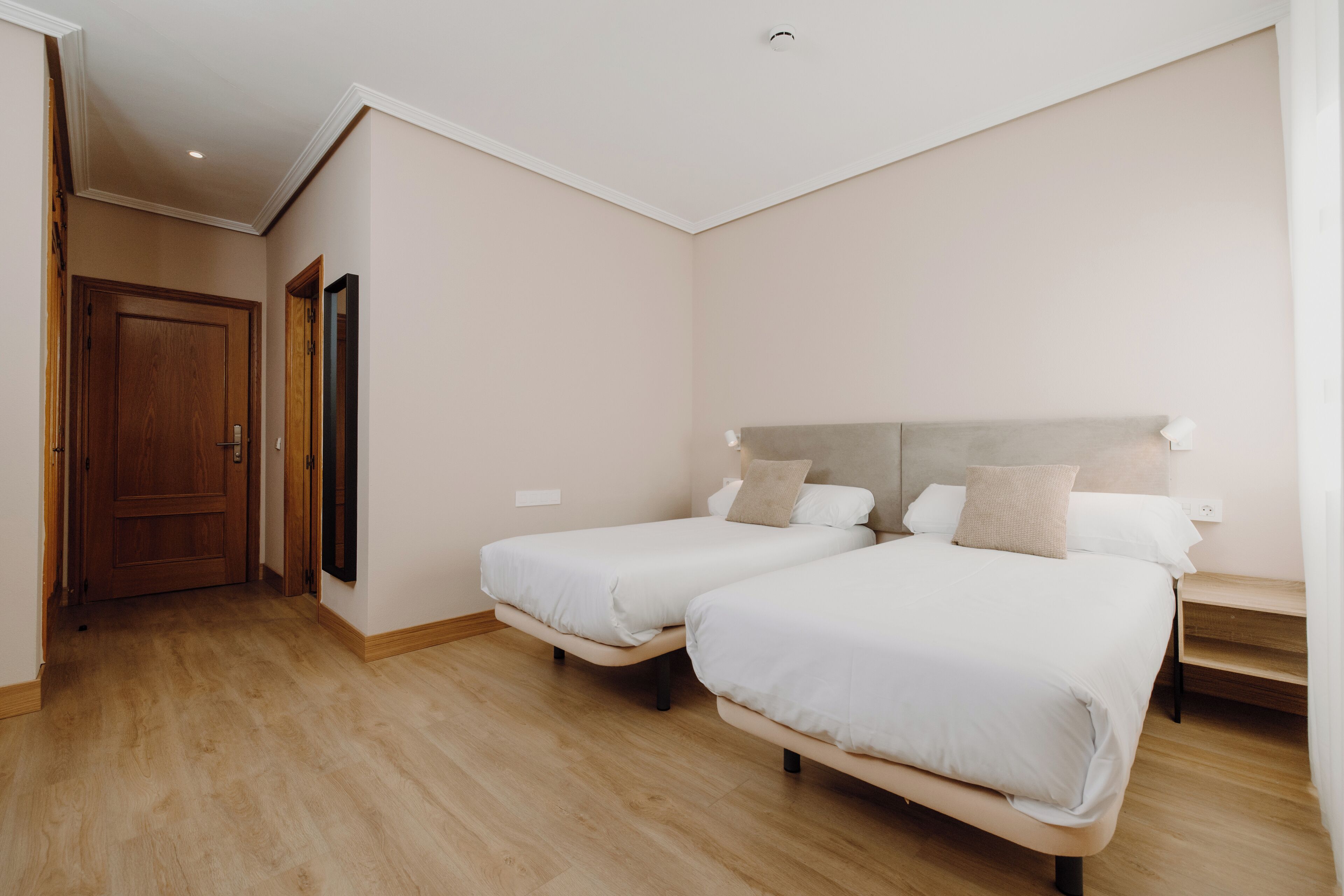 A bedroom with two beds, wooden flooring, and a door leading to another room.