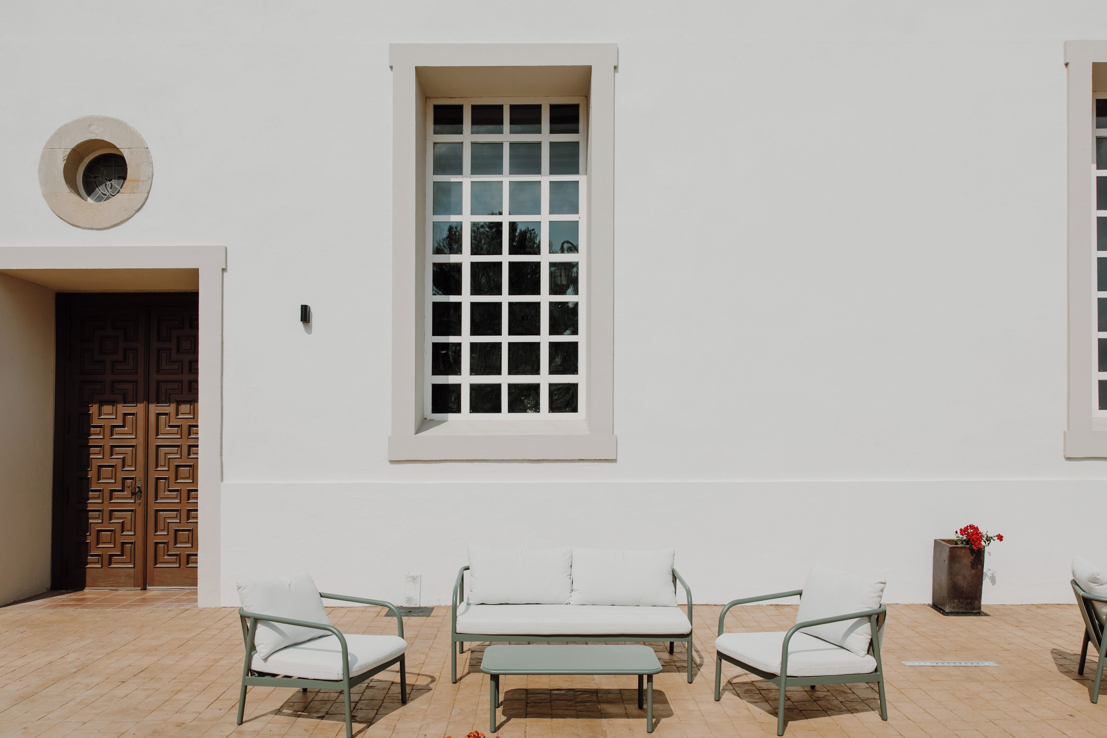Un patio con un muro blanco, un ventanal grande y un sofá con dos sillones.