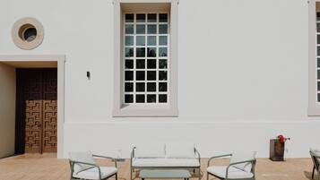 Un patio con un muro blanco, un ventanal grande y un sofá con dos sillones.