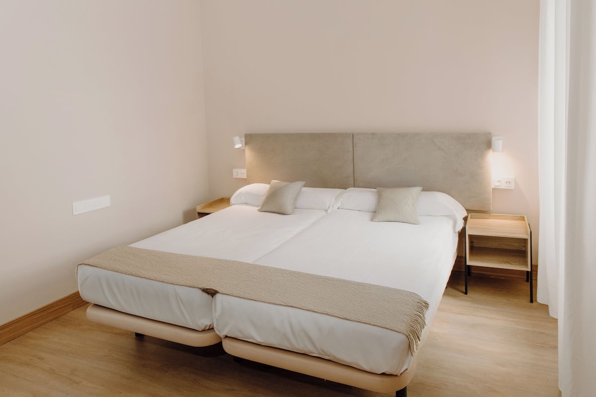 Una cama grande con cabecera, dos mesitas de noche y una lámpara de noche.