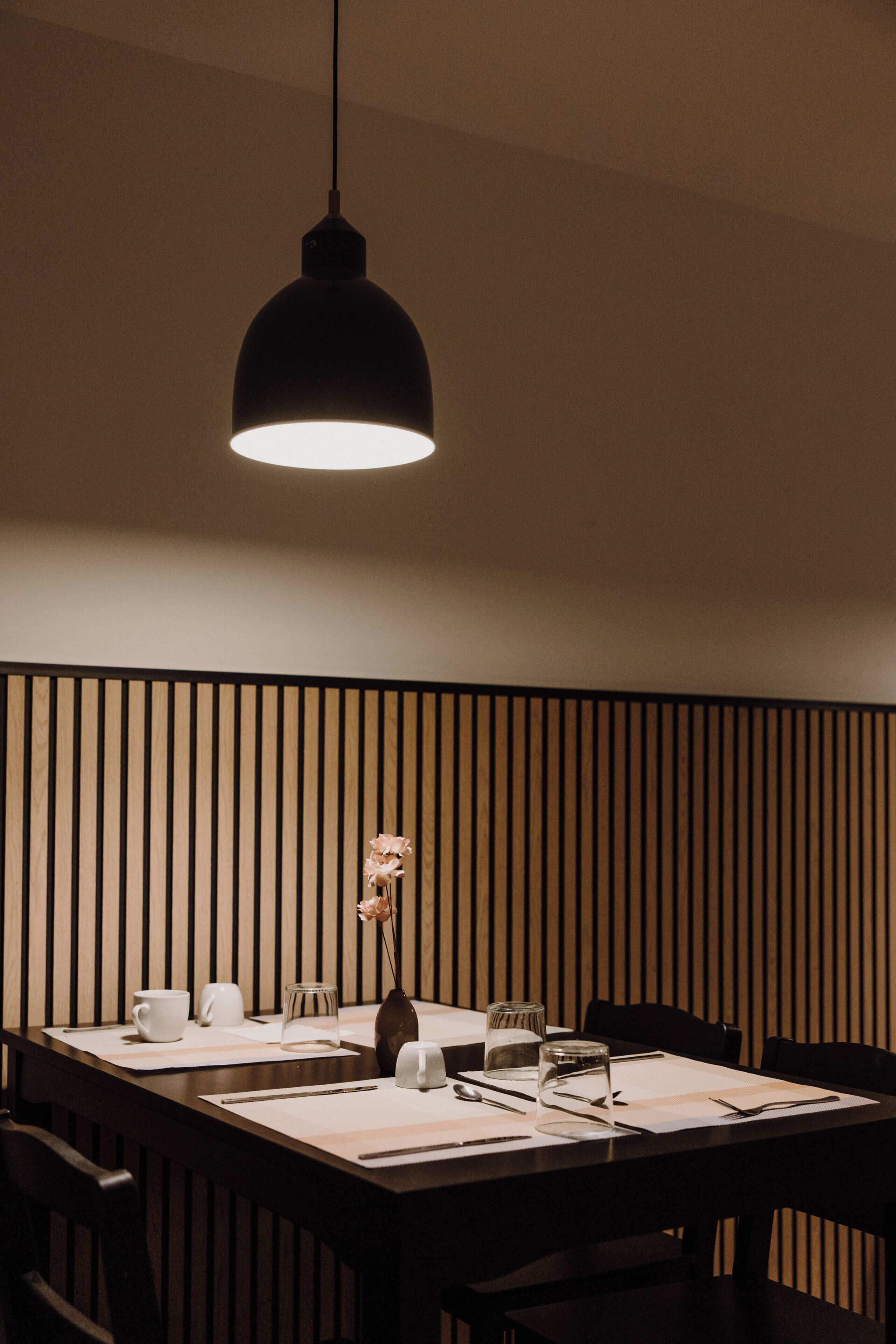 Een eetgedeelte met een tafel voor twee personen, een vaas met een enkele bloem, en een hanglamp.