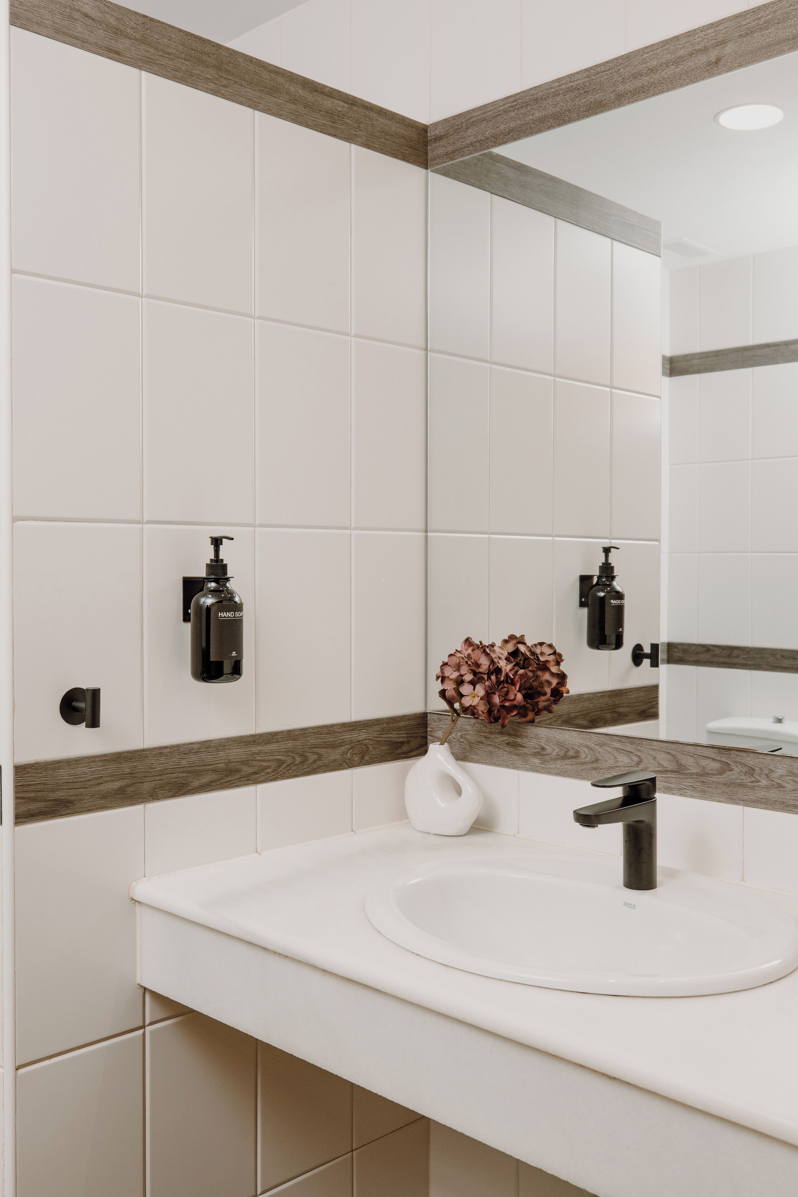 Un baño con lavamanos blanco, un espejo y dos dispensadores de jabón para manos.