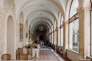 A corridor with arches, tables, chairs, and a chandelier. - Hotel Convento Miranda (Miranda de Ebro)