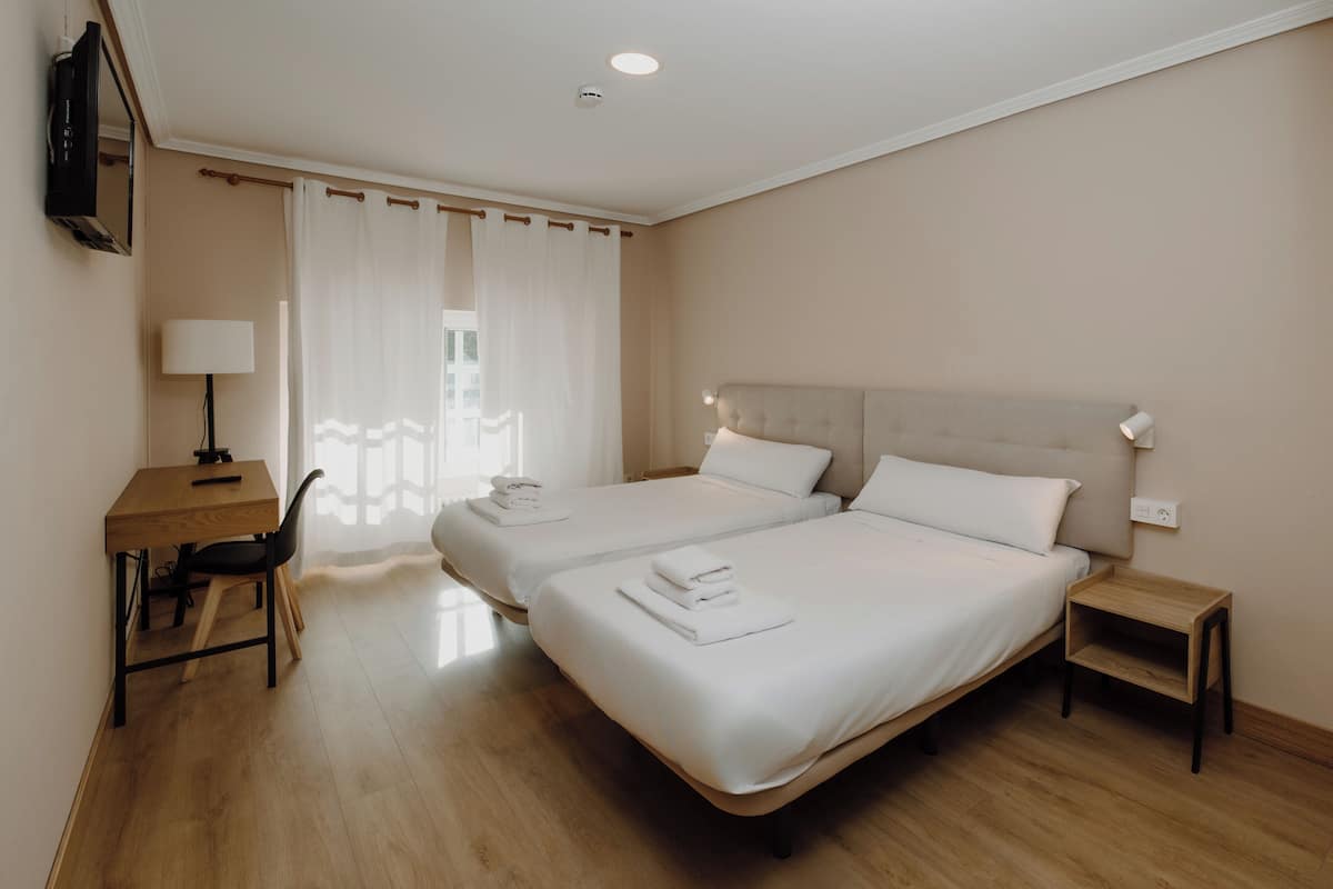 Habitación de hotel con dos camas, un escritorio, una silla, una lámpara y un televisor fijado a la pared.