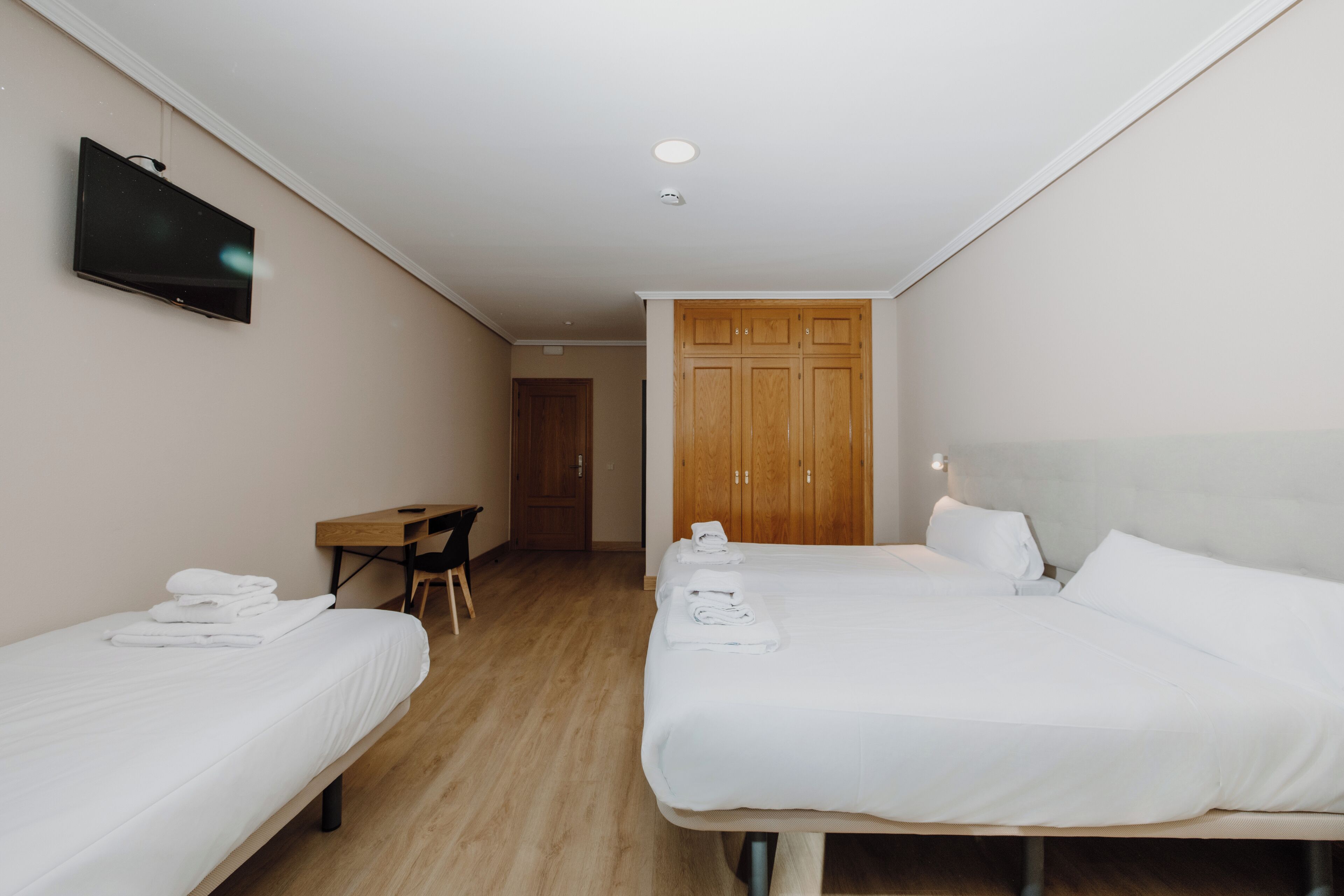 A hotel room with two single beds, a desk, a chair, a TV, and a wardrobe.