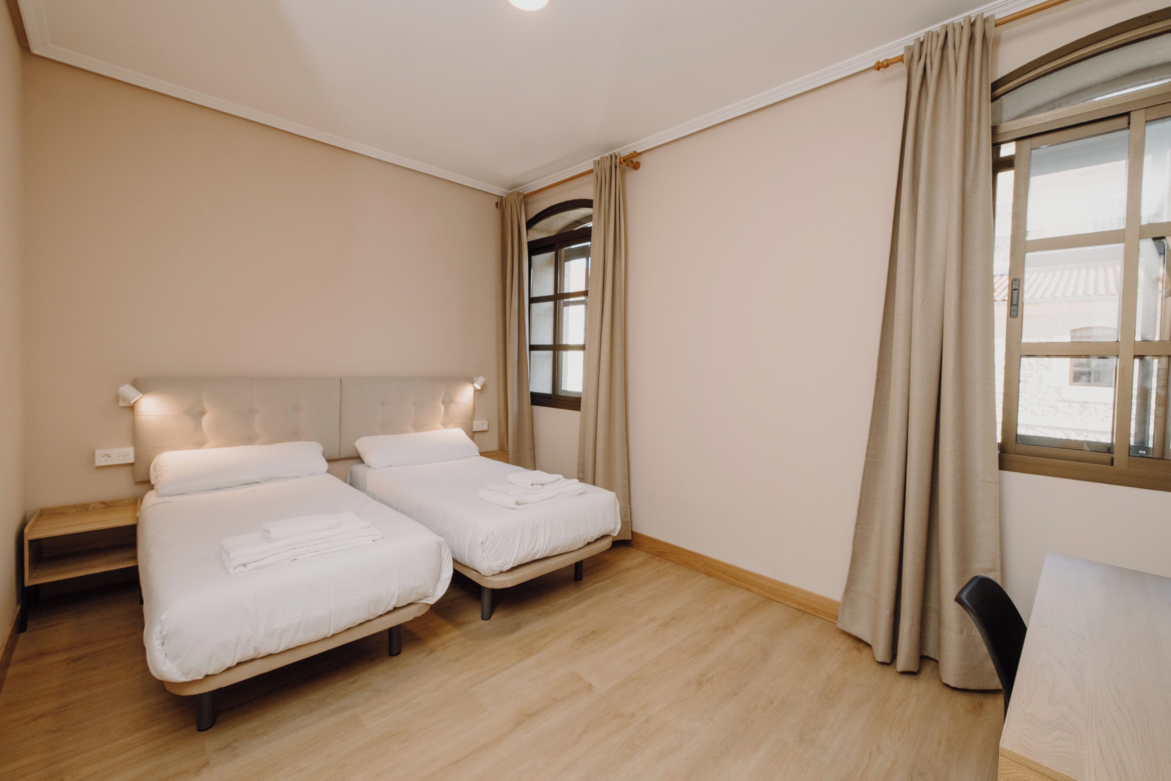 Une chambre d’hôtel avec deux lits, un bureau et une fenêtre avec des rideaux.