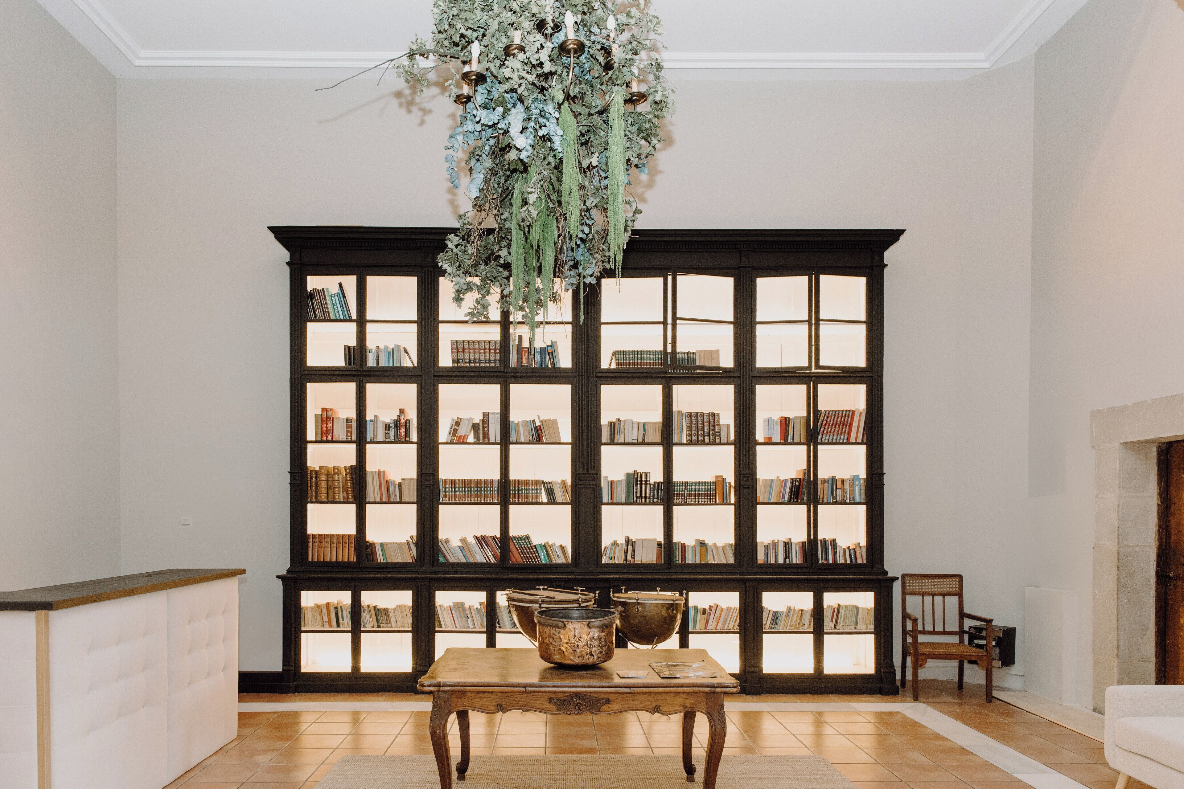Una habitación con una amplia estantería, una mesa de madera con un cuenco decorativo y una lámpara de araña con plantas colgantes.