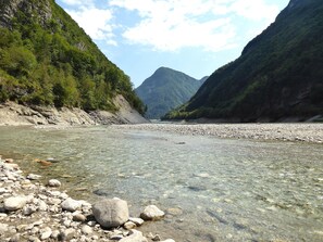 A clear river with rocky banks and lush green mountains in the background. - Chalet Giove (Belluno)