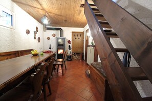Een landelijke keuken met een houten tafel, stoelen, een houtkachel en een wenteltrap.