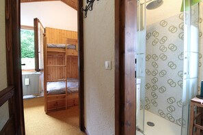 Een kamer met stapelbedden, een douche met betegelde wanden en uitzicht op groen buiten.