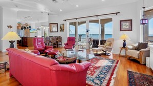A spacious living room with a red sofa, a glass coffee table, and a view of the ocean through large windows.