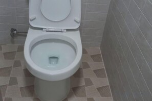 A toilet with a closed lid in a bathroom with patterned tiles. - Adam Guesthouse (Gyeongju)