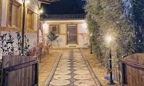 Ein Weg führt zu einem Gebäude im traditionellen Stil, umzäunt mit einem Holzzaun, und hat einen gut beleuchteten Eingang.